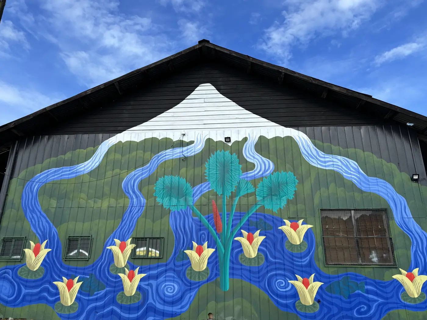Mural de Michael Yaikel en el Galpón Estación: un volcán nevado, ríos azules y flores amarillas